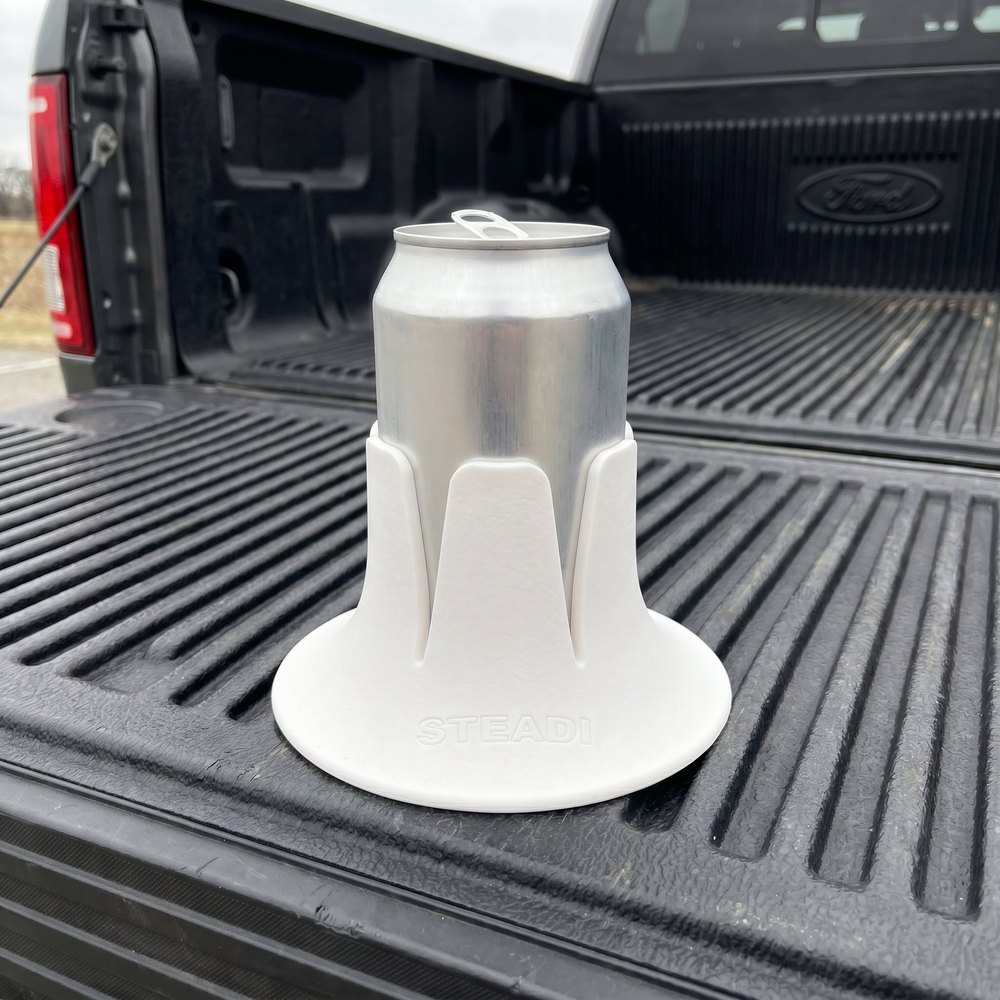 A plain aluminium can standing in a white Steadi on the ribbed bed liner of an open truck tailgate.